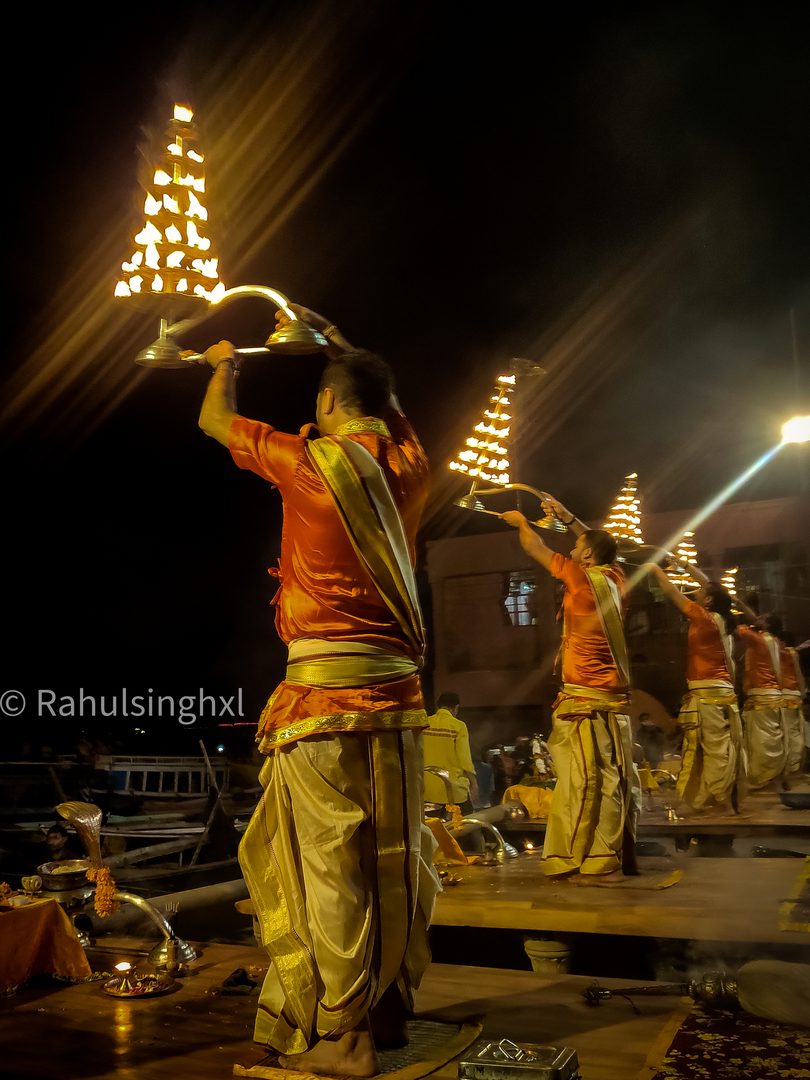 Priests lifting multi-tiered flaming brass lamps during evening Ganga Aarti ritual