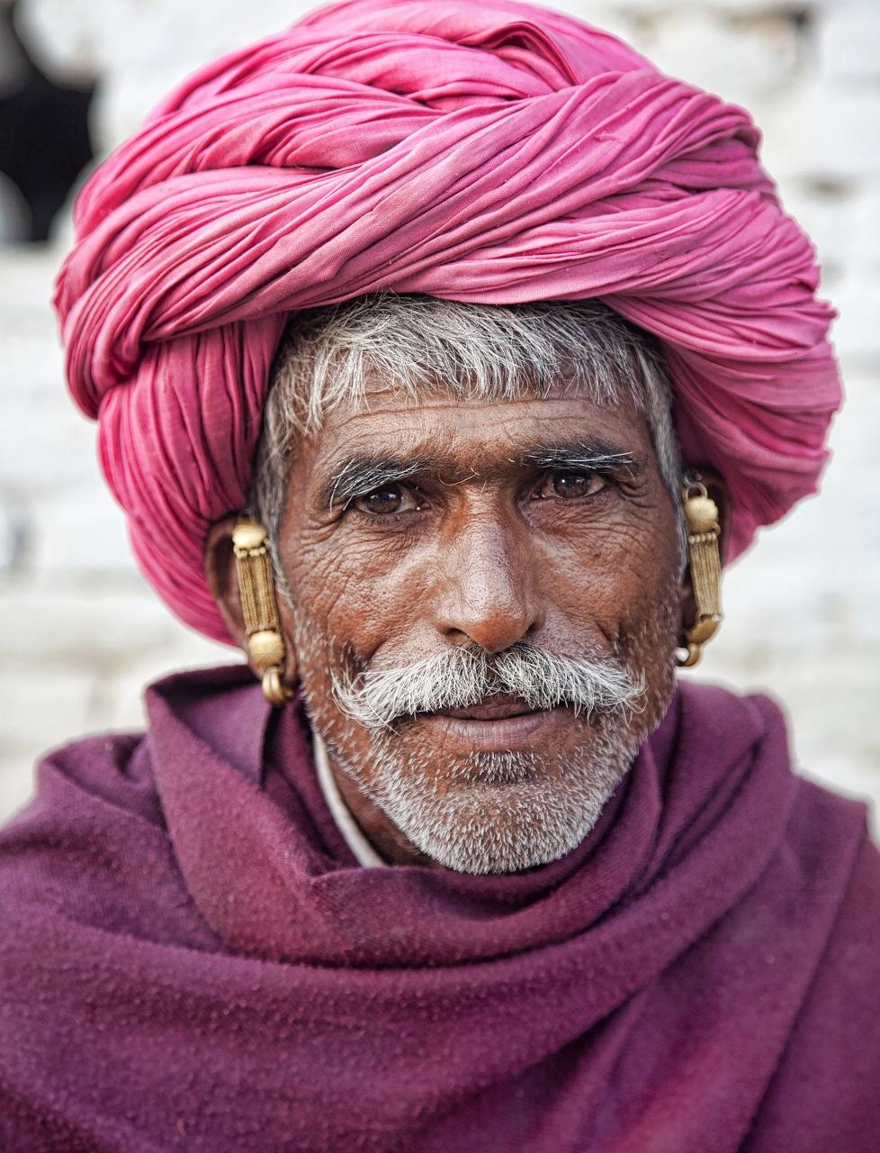 Portrait of an elder Rajasthani artisan with deep character, weathered smile and red turban