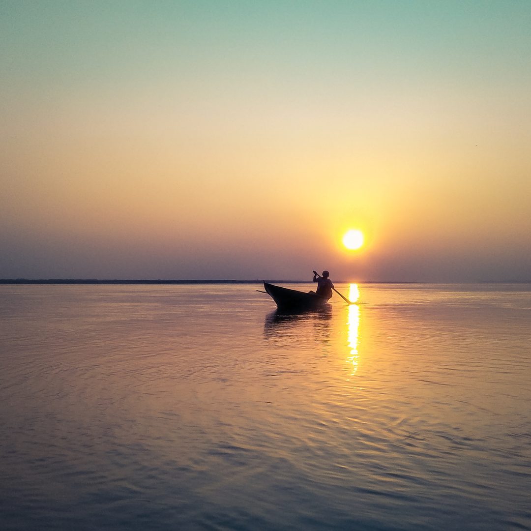 Traditional wooden country boat resting on the golden silt shores of the mighty Brahmaputra River in Assam