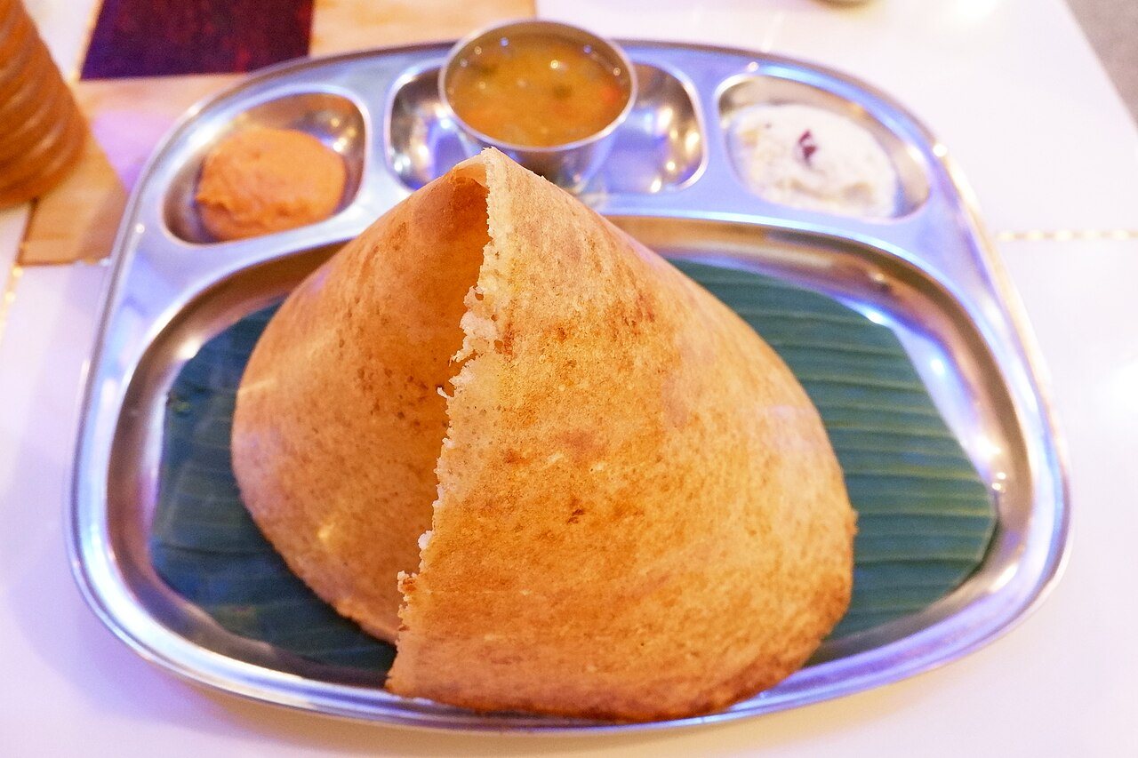 Crisp golden masala dosa served on fresh green banana leaf with coconut chutneys and hot sambar
