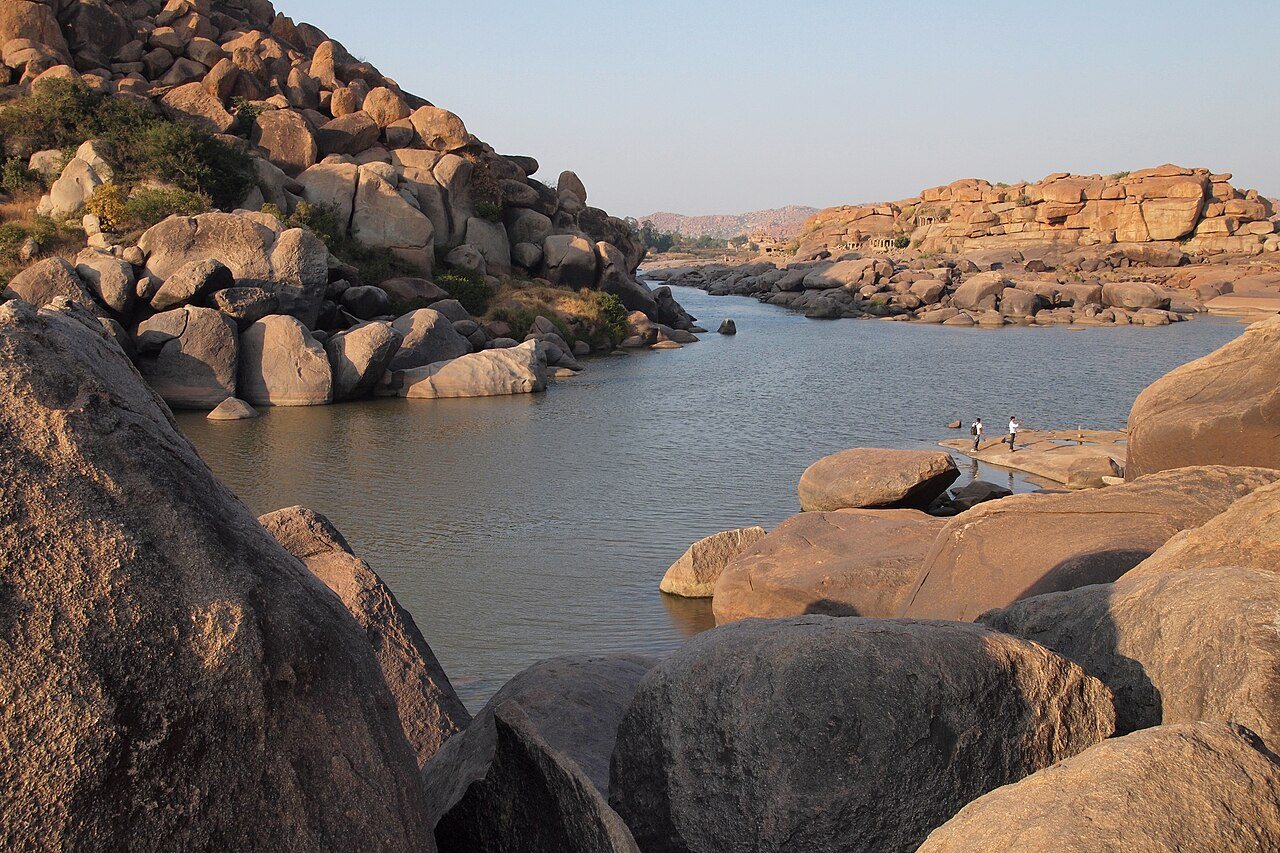 Round wicker coracle floating on the sacred Tungabhadra River beside massive Hampi granite boulders