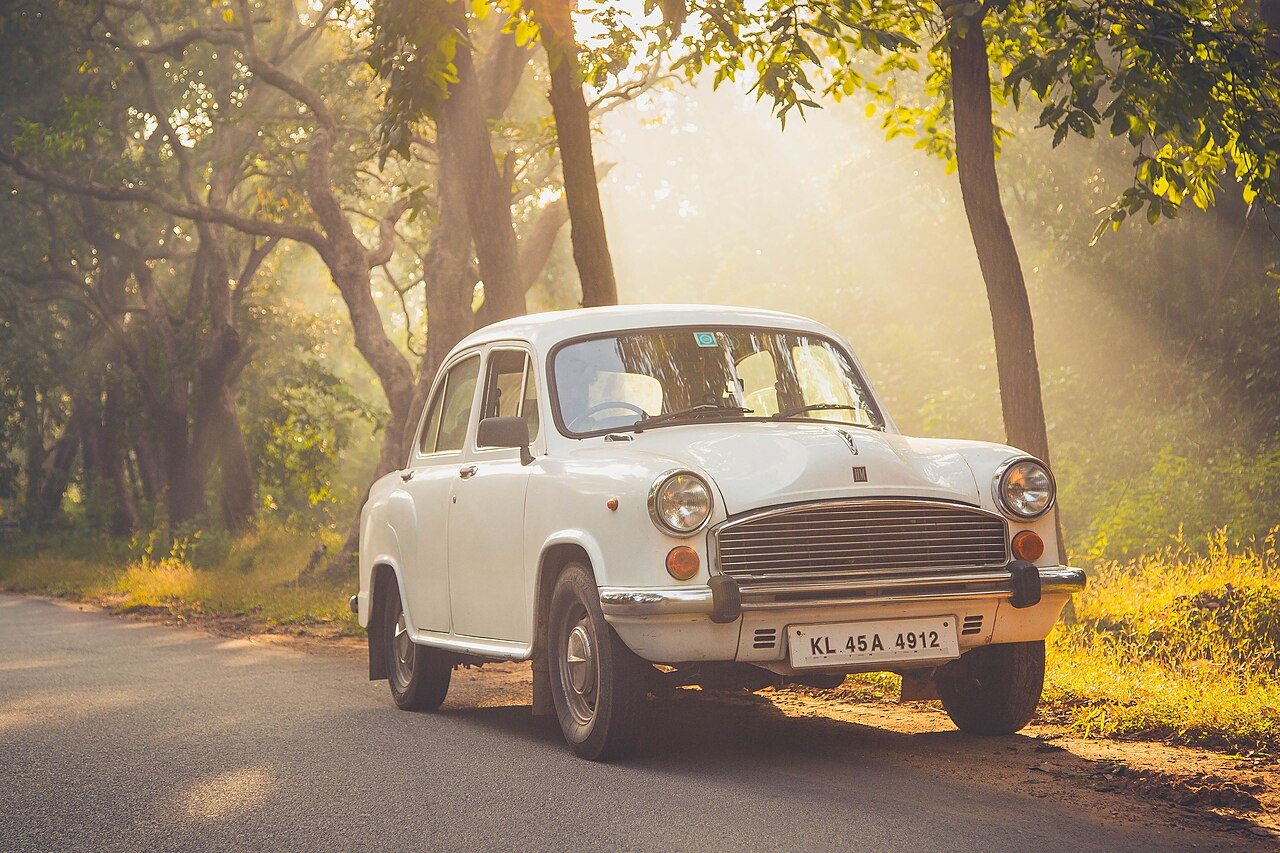 Classic yellow Ambassador taxi on tree-lined street in North Kolkata